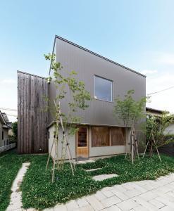 金属サイディング、塗り壁、魚沼杉を組み合わせた外観。正面が店舗の入口で、住居の玄関は左奥の目立たない場所に配されている。