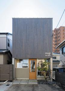 グレーに塗装された杉板の壁が印象的な外観。ヘアサロンの木製ドアがかわいい。住居の入口は左手にある。