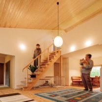 勾配天井のリビングが住まいの中心。床だけでなく天井の羽目板や階段も杉材で統一されている。漆喰壁の陰影も味わい深い。